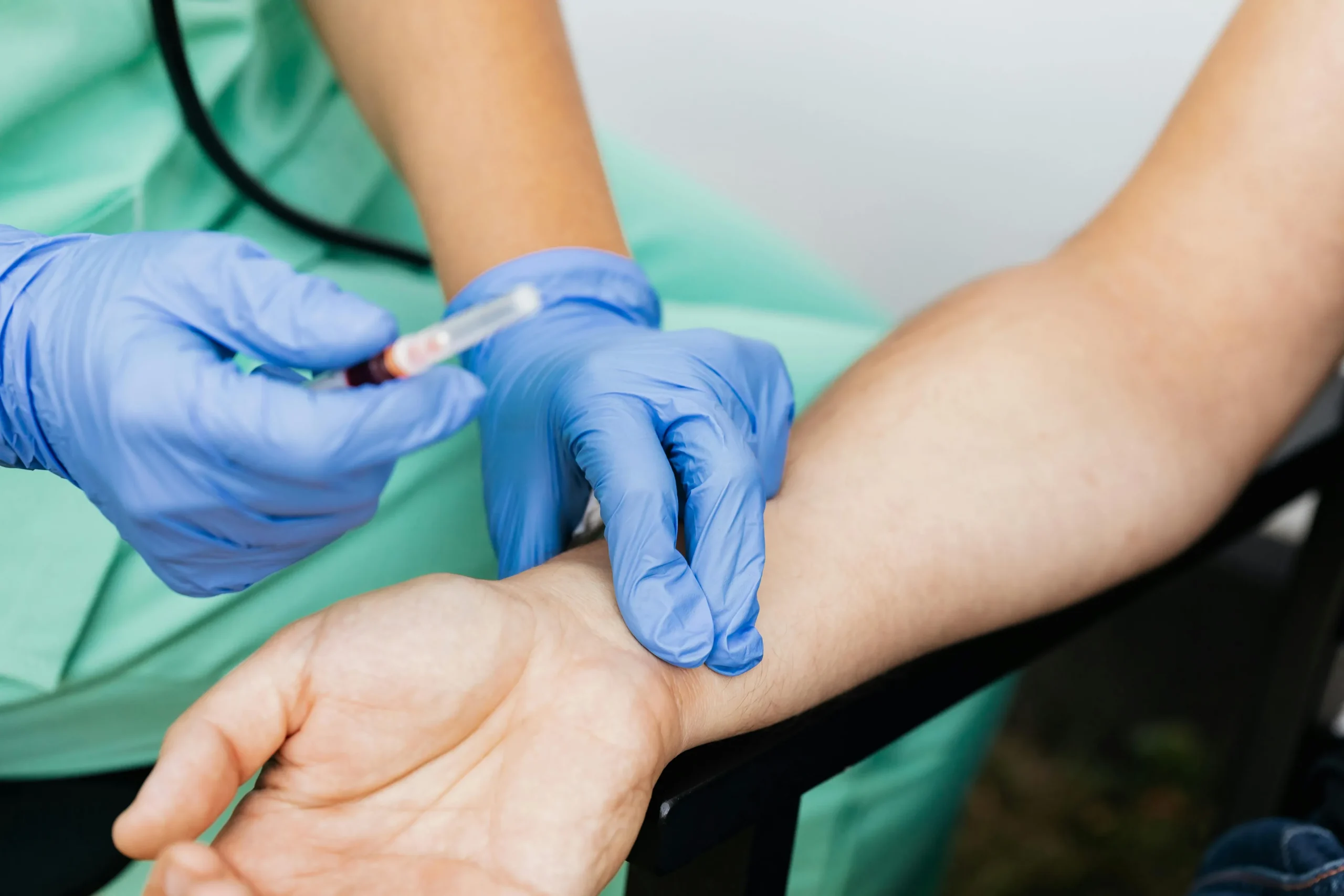 Healthcare professional wearing blue latex gloves performing a blood draw or venipuncture on a patient's arm for genetic testing and biomarker analysis.
