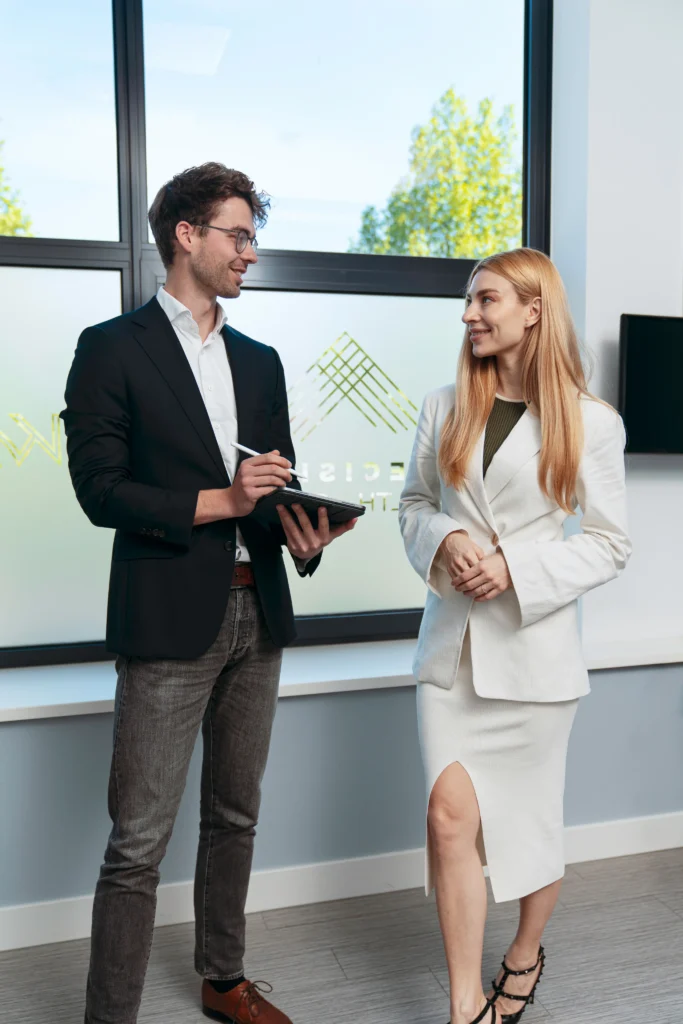 Man and woman in business attire examining a tablet together in a contemporary office with natural light and geometric branding